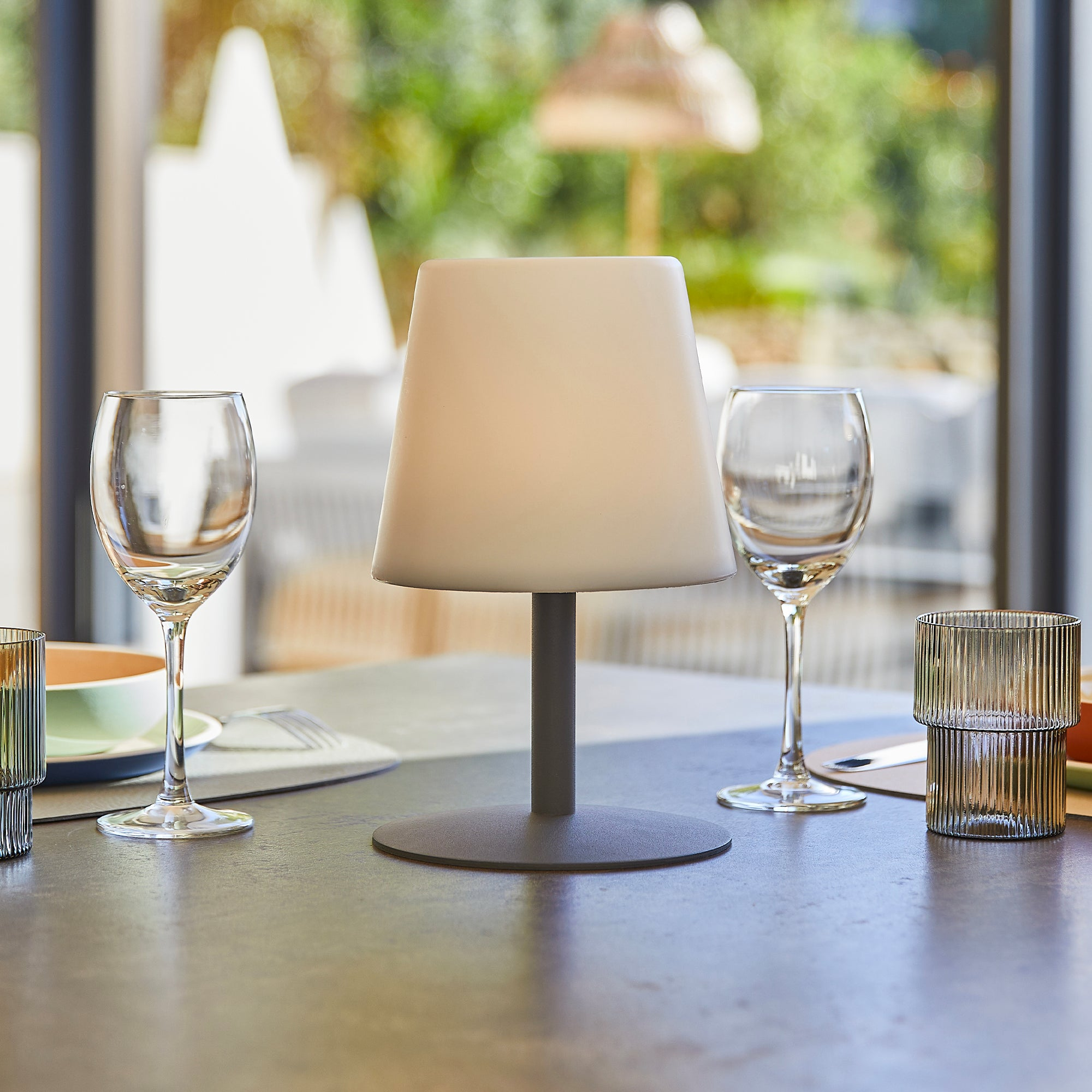 Ein Tisch mit Gläsern, einer Lampe und Geschirr im Freien.