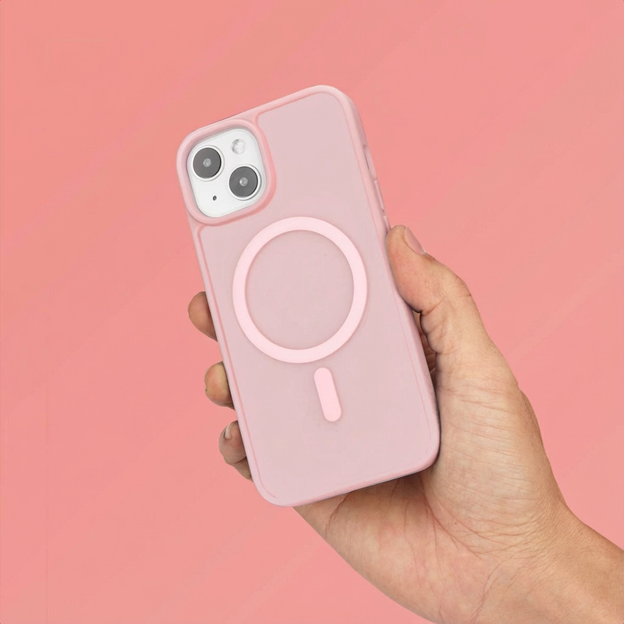 Een hand houdt een roze telefoon met cameramodule en magneetring vast.