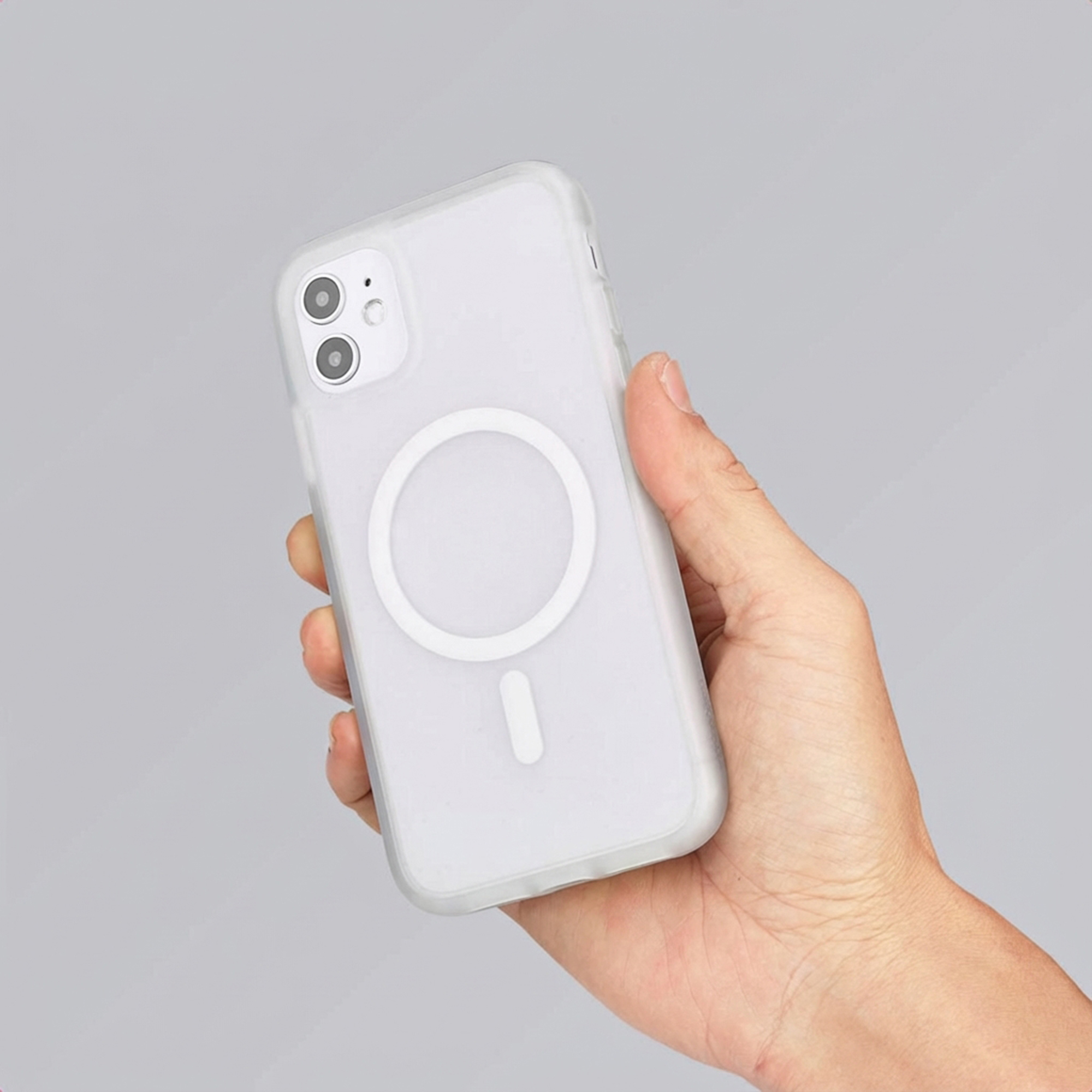 Een hand houdt een witte smartphone met doorzichtige hoes vast. MagSafe-ring zichtbaar.