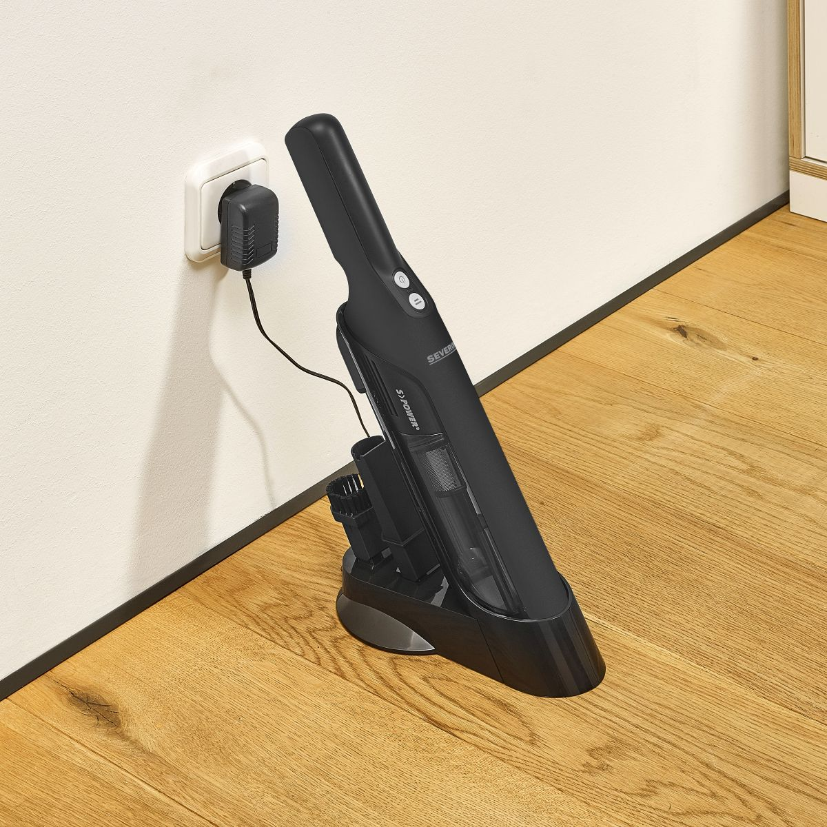 Aspirateur noir portatif en charge dans une prise murale.