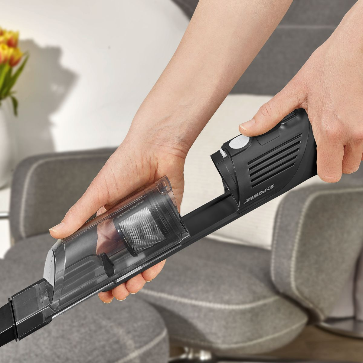 Des mains tiennent un aspirateur noir pour vider le bac à poussière.