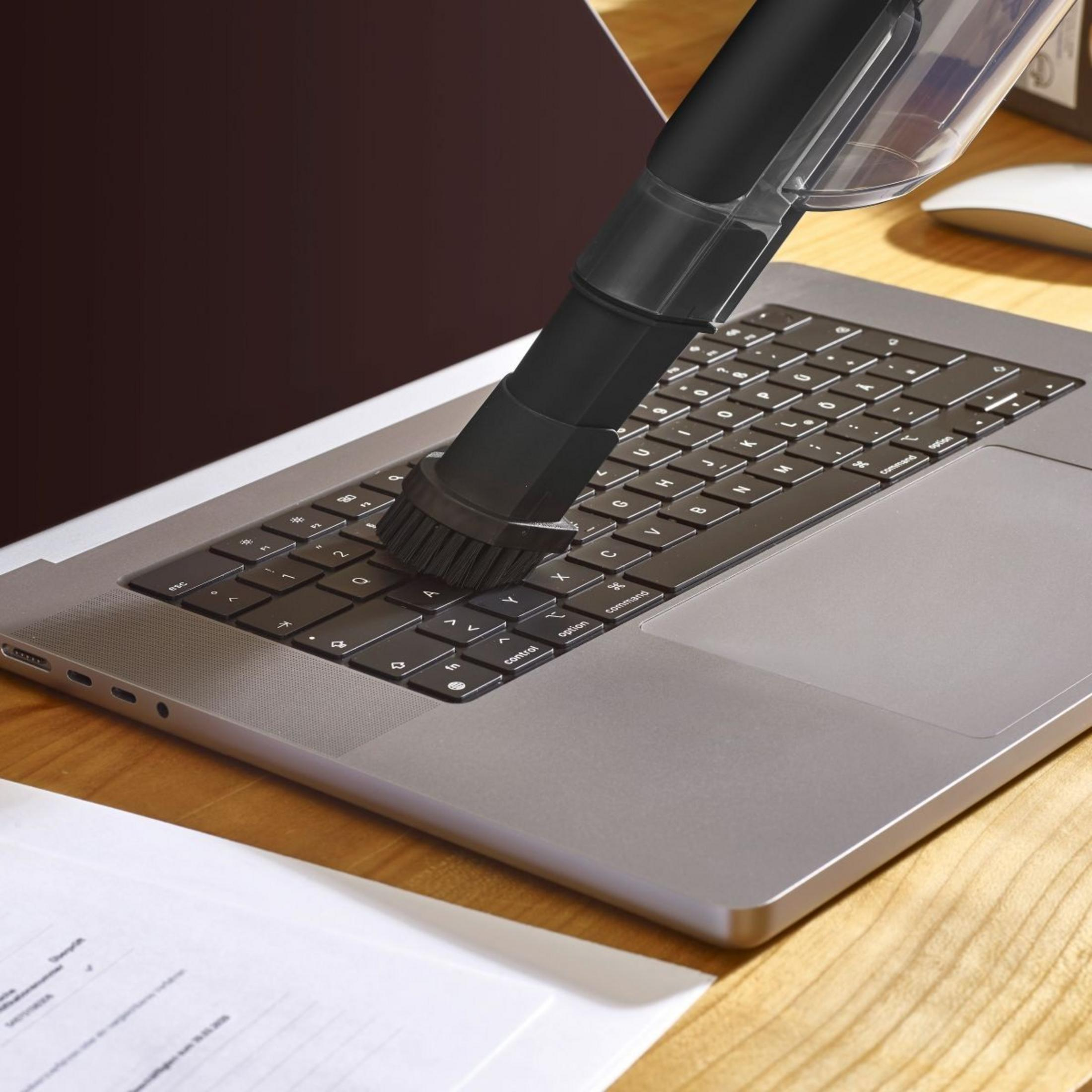 Un aspirateur à main nettoie le clavier d'un ordinateur portable sur un bureau en bois.