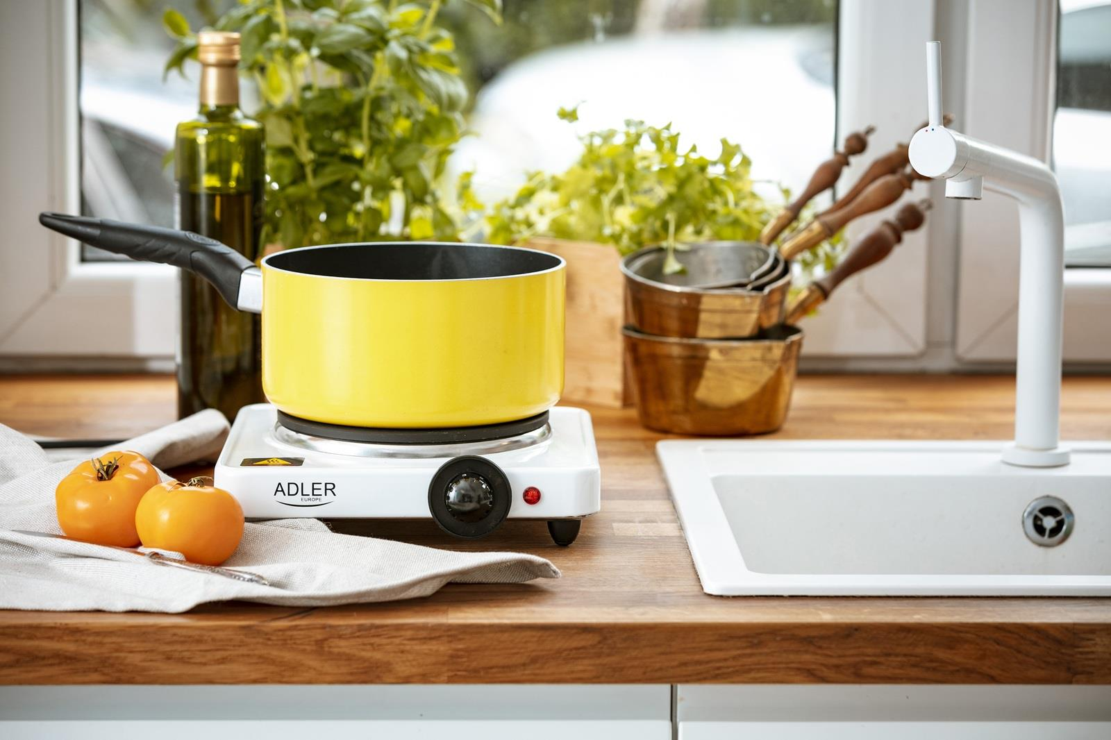 Żółty garnek na płycie grzewczej z pomidorami i oliwą z oliwek obok zlewu.