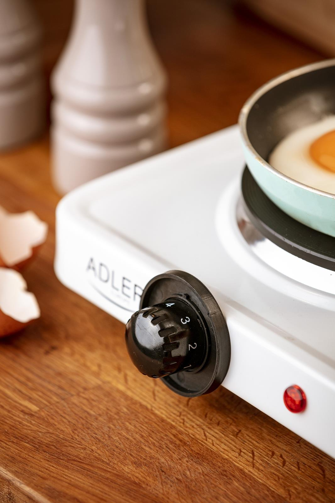 Jajko sadzone smaży się na patelni na białej płycie grzewczej z czarnym pokrętłem.