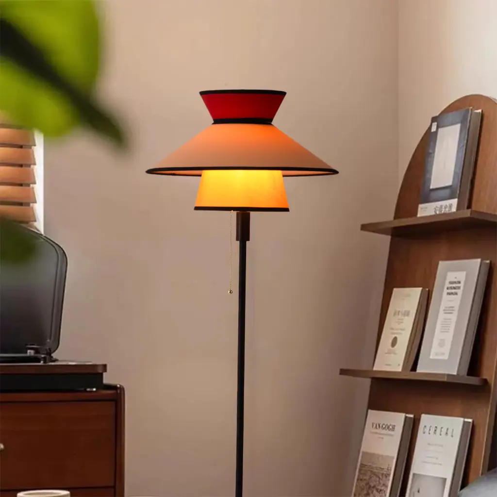 Una lámpara de pie con pantallas roja y naranja está junto a una estantería.