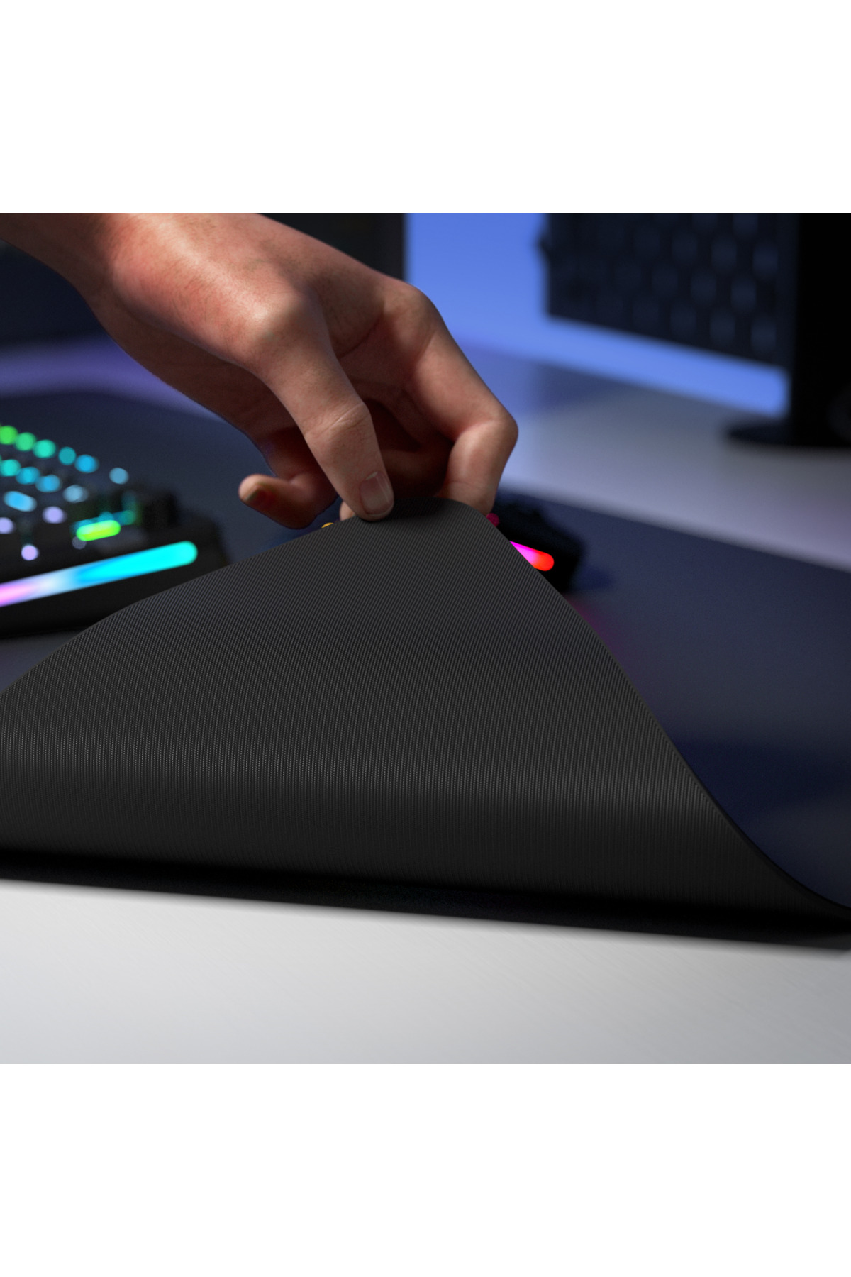 Eine Hand hebt eine schwarze Mauspad-Ecke an. RGB-Tastatur im Hintergrund.