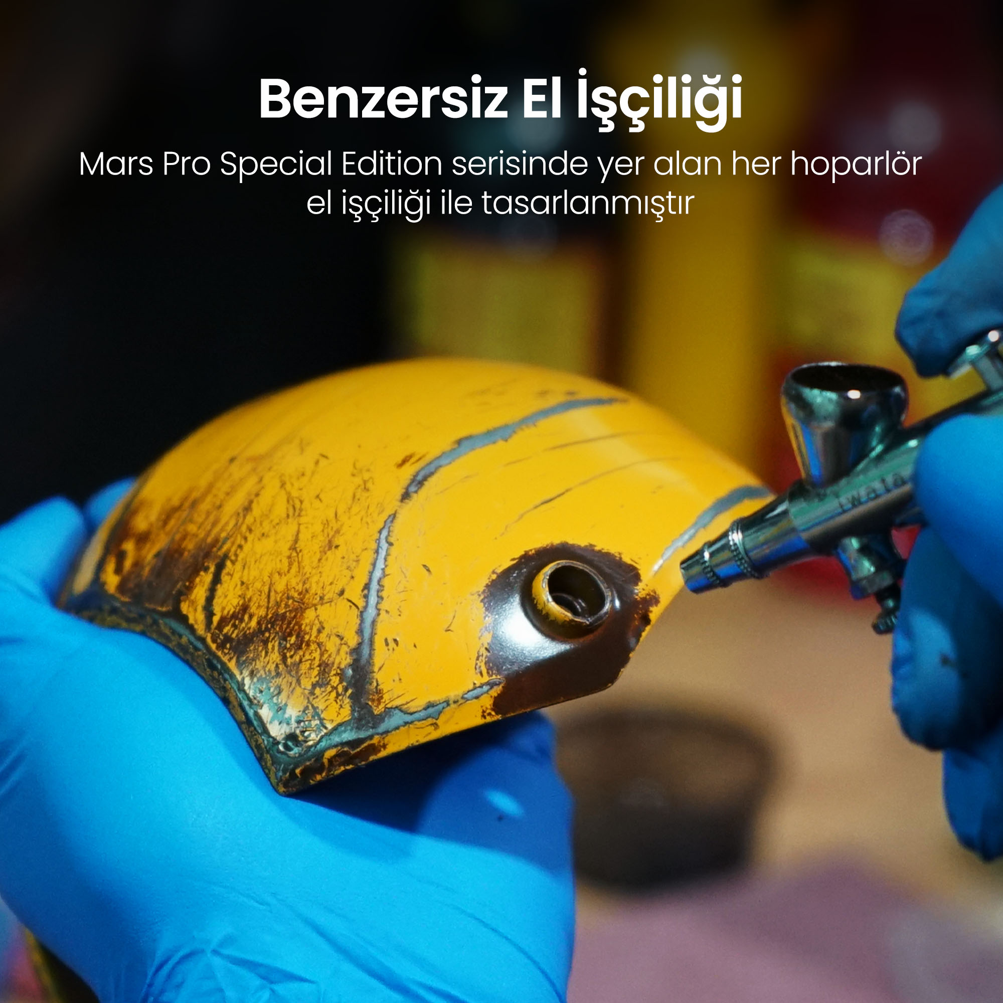 Mavi eldivenli kişi, airbrush tabancasıyla sarı parçayı tutuyor.