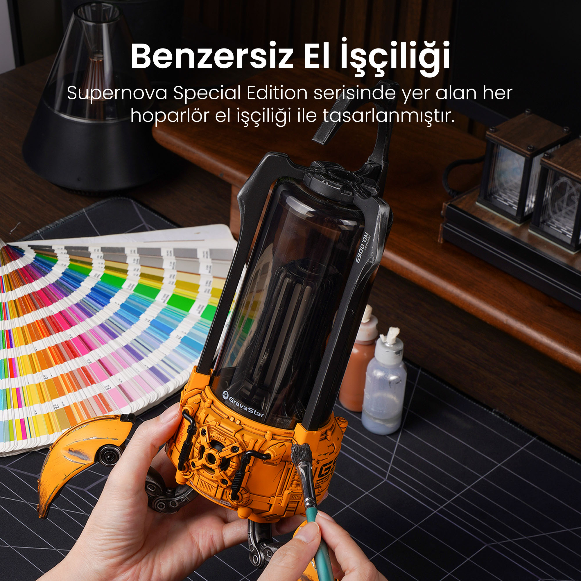 Ręka maluje pomarańczowy głośnik pędzlem obok wachlarza próbek kolorów.