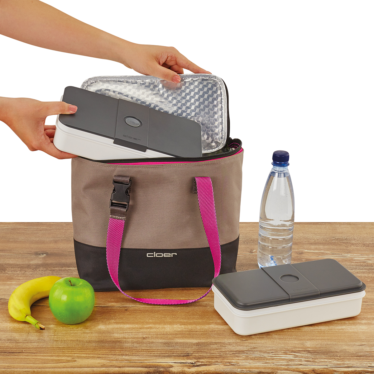 Eine Tasche mit Brotdosen, Obst und Wasser auf einem Holztisch.