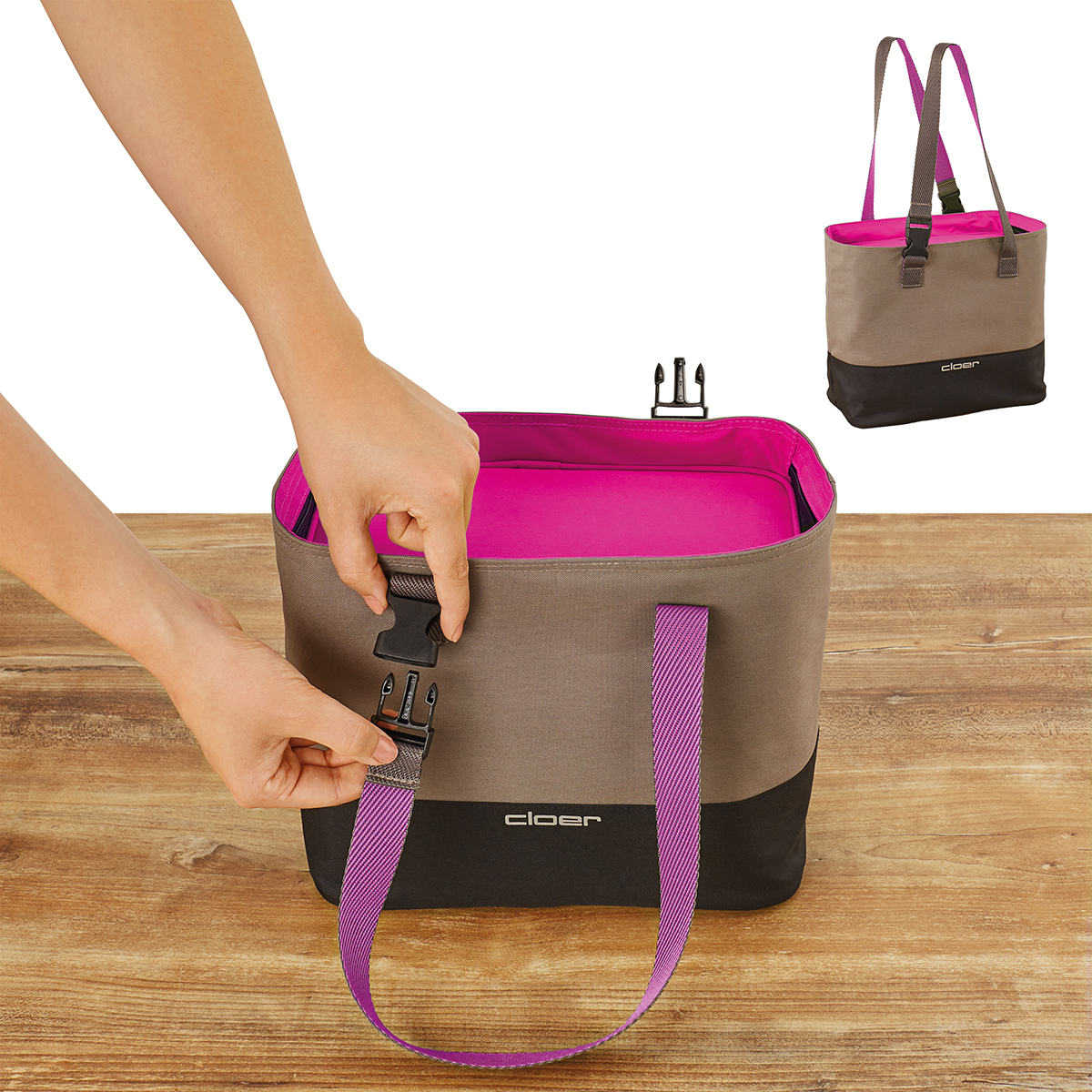 Eine Hand schließt eine braune Tasche mit pinkem Innenfutter und lila Trägern auf einem Holztisch.