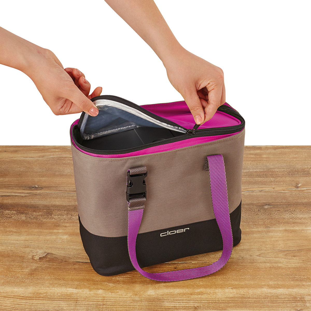 Eine graubraune Kühltasche mit pinkem Reißverschluss und Henkeln wird geöffnet.