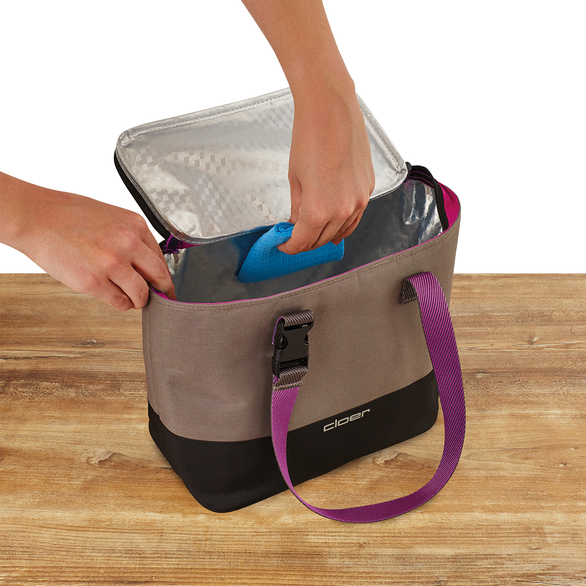 Person legt blaues Kühlpack in graue Kühltasche mit lila Trägern.
