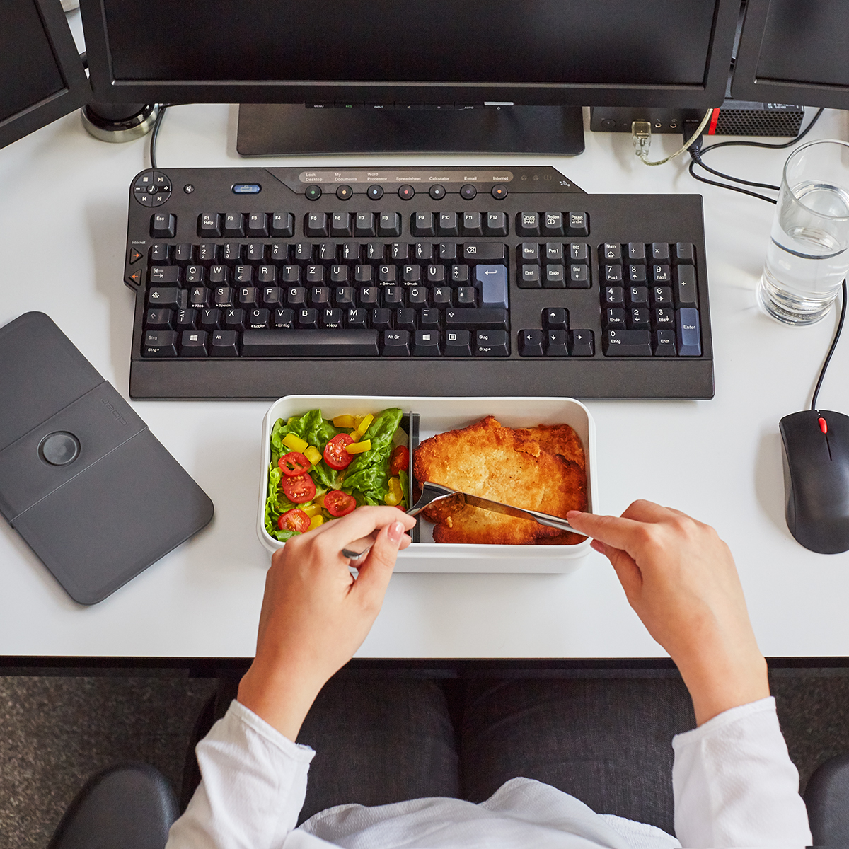 Eine Person isst in der Nähe einer Tastatur und eines Computers. Mittagessen im Büro.