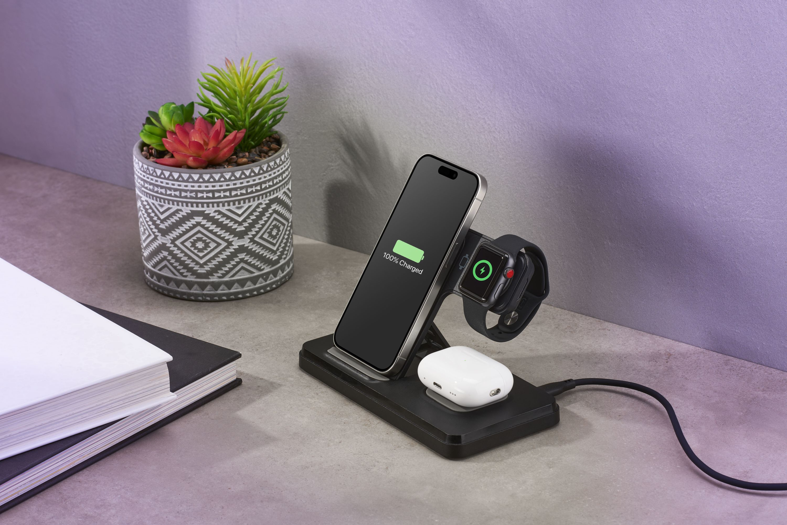 Estación de carga con teléfono, reloj y audífonos. Al lado, una maceta con suculentas.