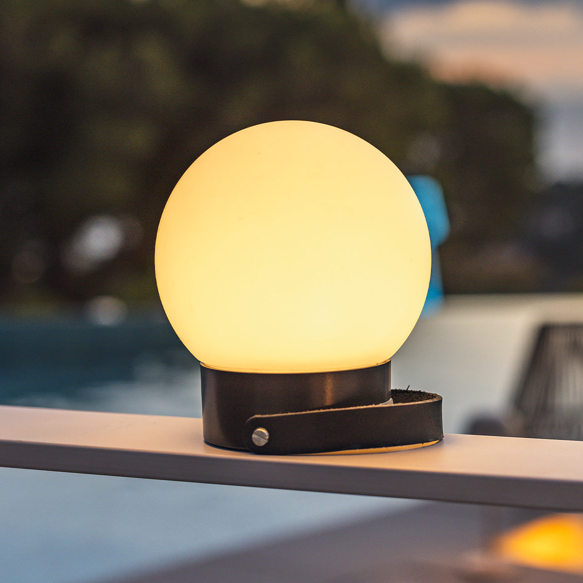 Eine leuchtende, kugelförmige Lampe mit schwarzem Sockel auf einer Reling.