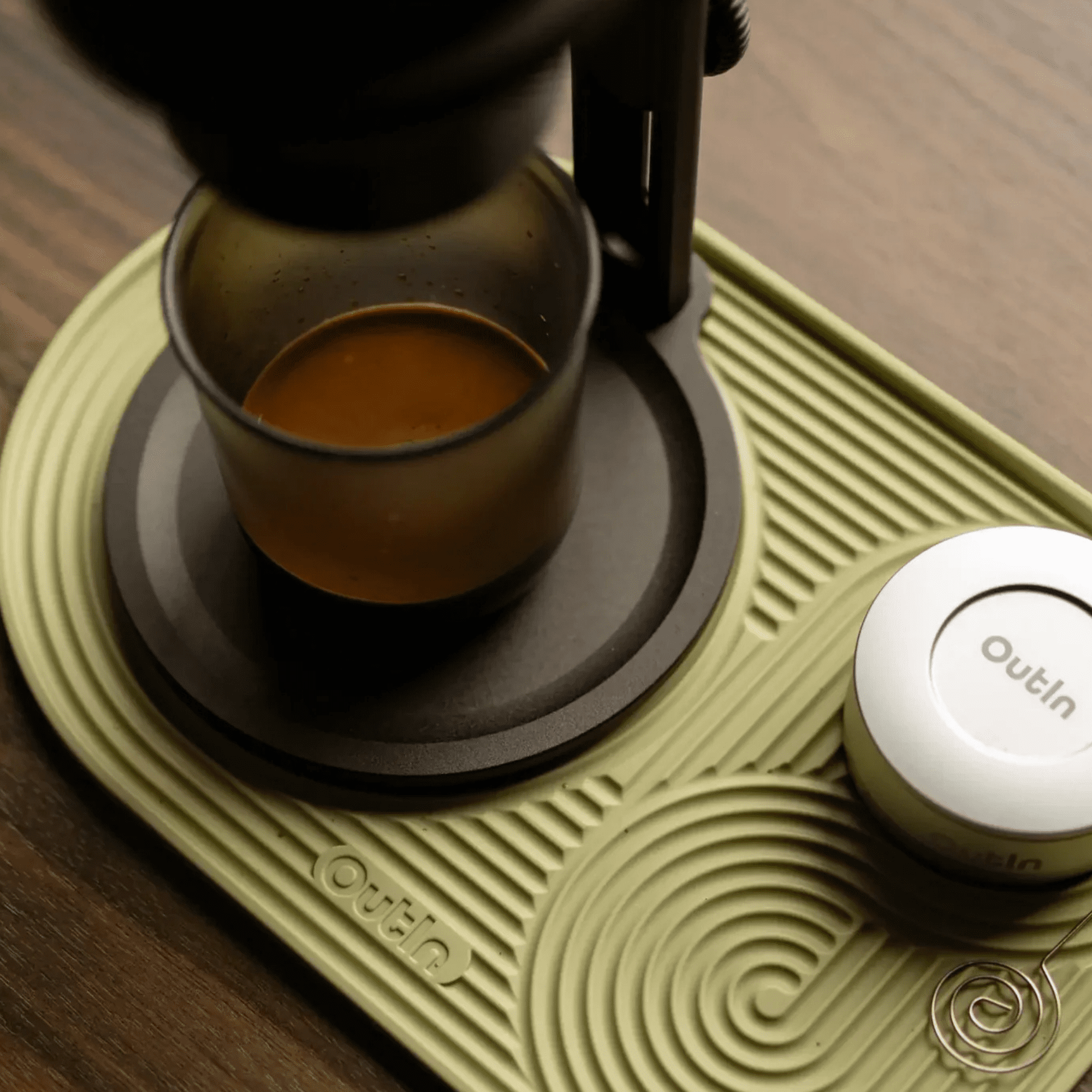 Eine Espressomaschine brüht Kaffee in ein Glas auf einer olivgrünen Matte.
