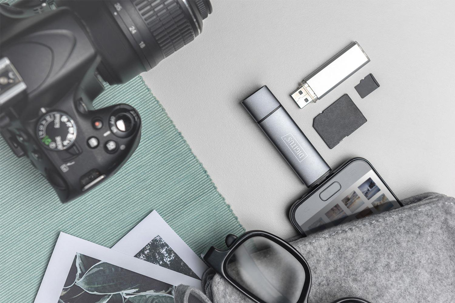 Eine Kamera, ein USB-Stick, SD-Karten, ein Handy, Brille und Fotos liegen auf Stoff.