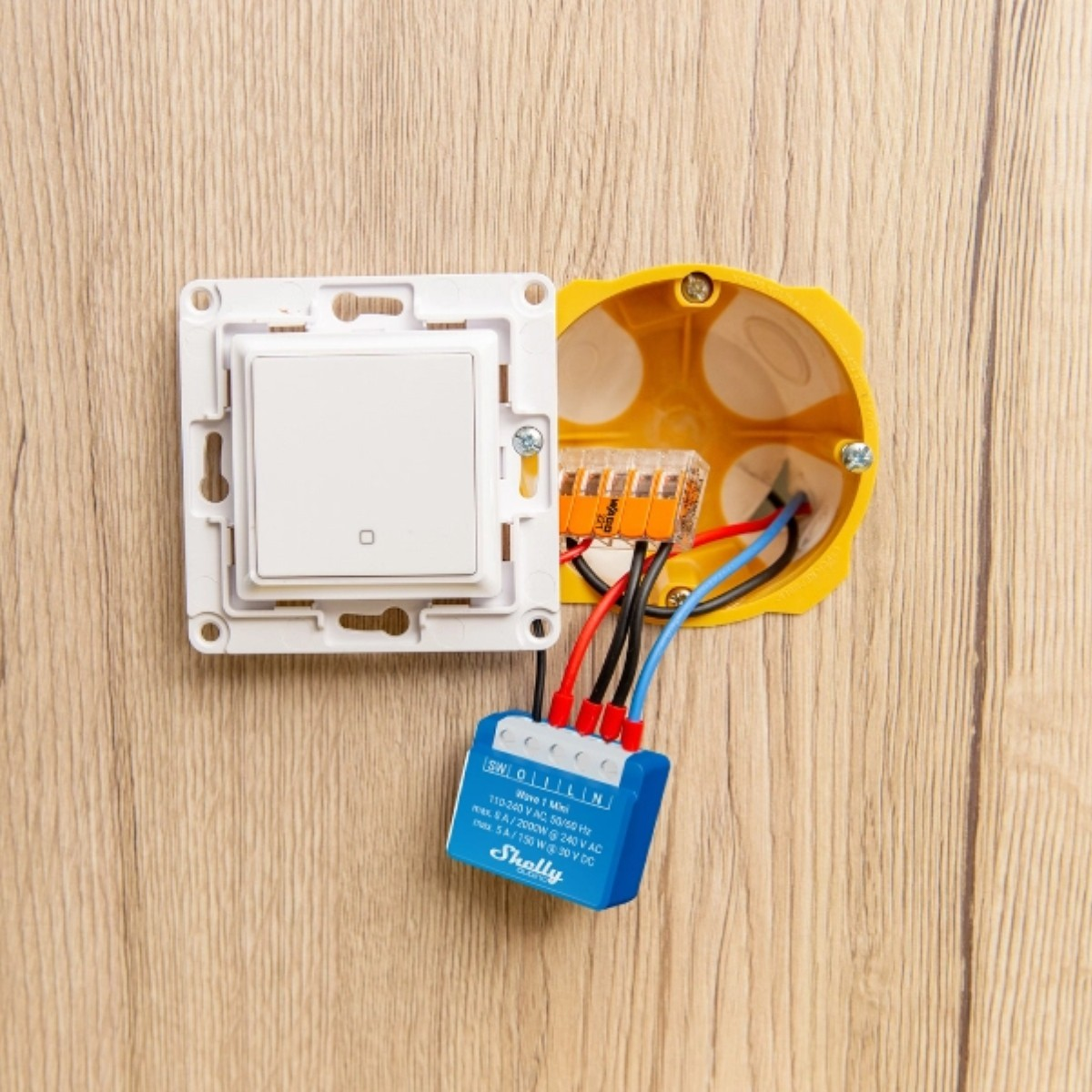 Un interruptor de luz blanco está conectado a un pequeño dispositivo Shelly azul y conectores WAGO.
