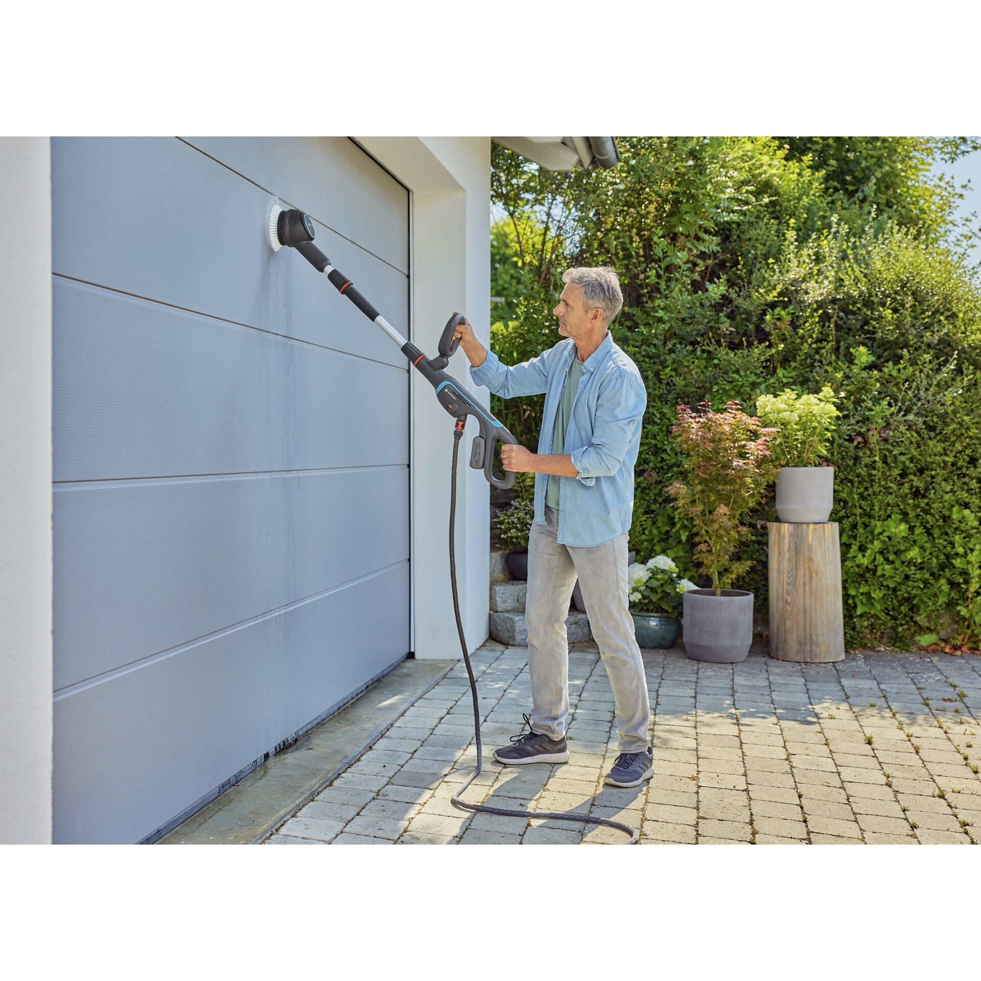 Un uomo pulisce una porta del garage con idropulitrice e spazzola.