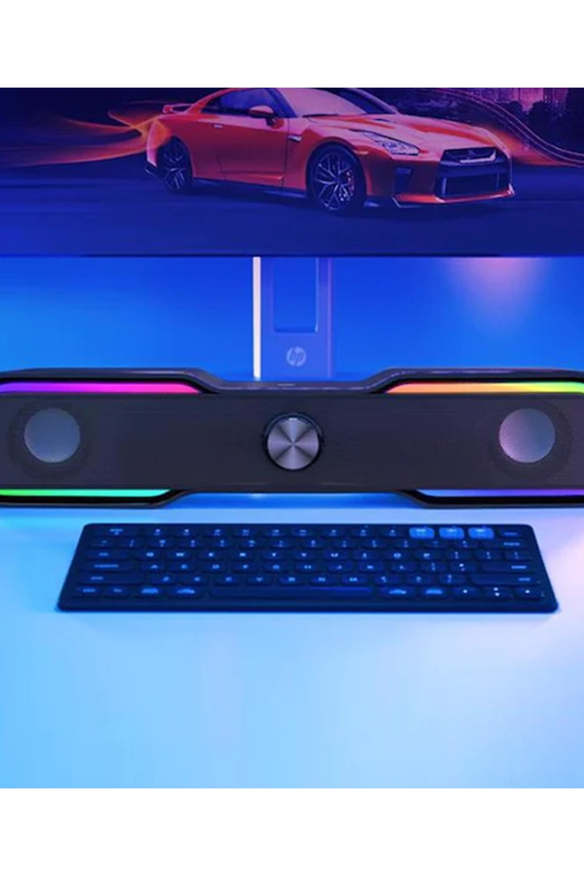 Czerwony samochód przed monitorem komputerowym z listwą dźwiękową i klawiaturą.