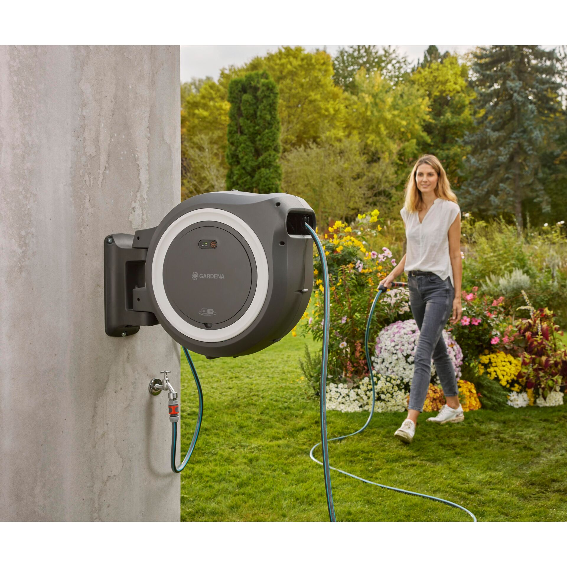 Frau mit Gartenschlauch im Garten neben einer Wandmontage-Schlauchbox.