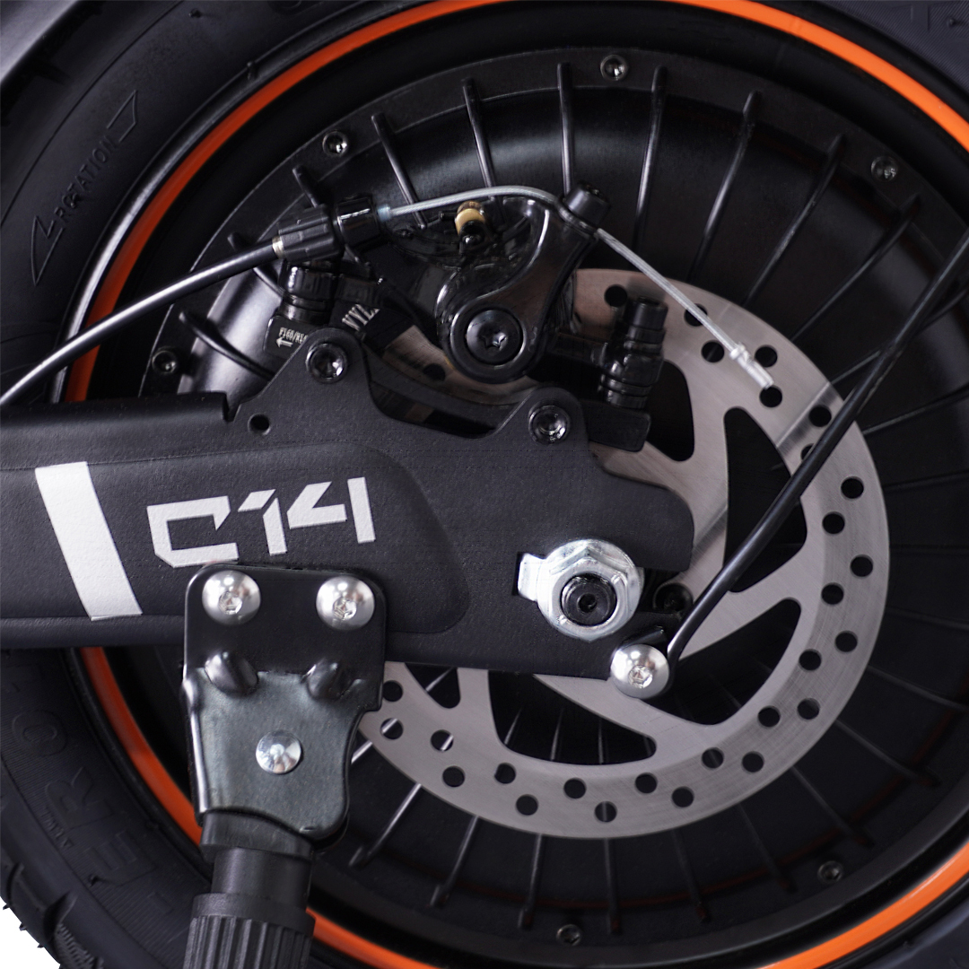 Zbliżenie tylnego koła hulajnogi, pokazujące tarczę hamulcową i detale pomarańczowej obręczy.