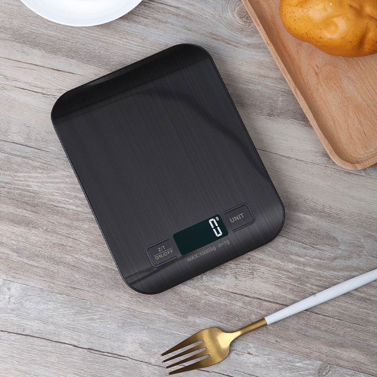 Czarna waga cyfrowa z pustym wyświetlaczem na drewnianym stole. W pobliżu ziemniak i widelec.