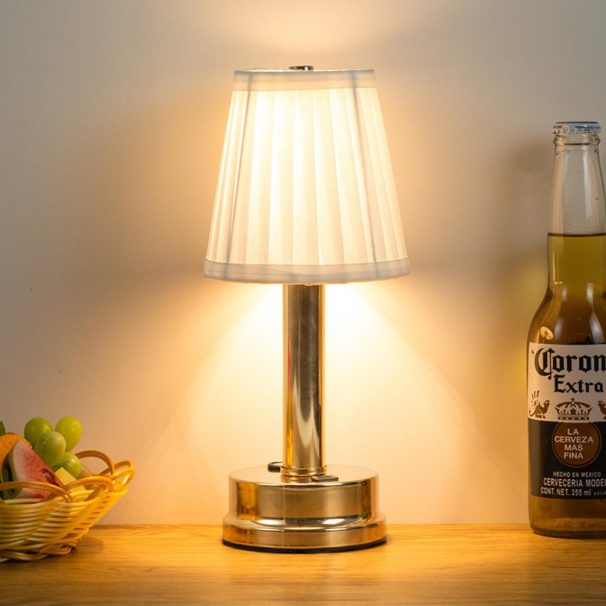 Eine goldene Lampe mit weißem Schirm steht neben einer Flasche Corona Extra und Obst.