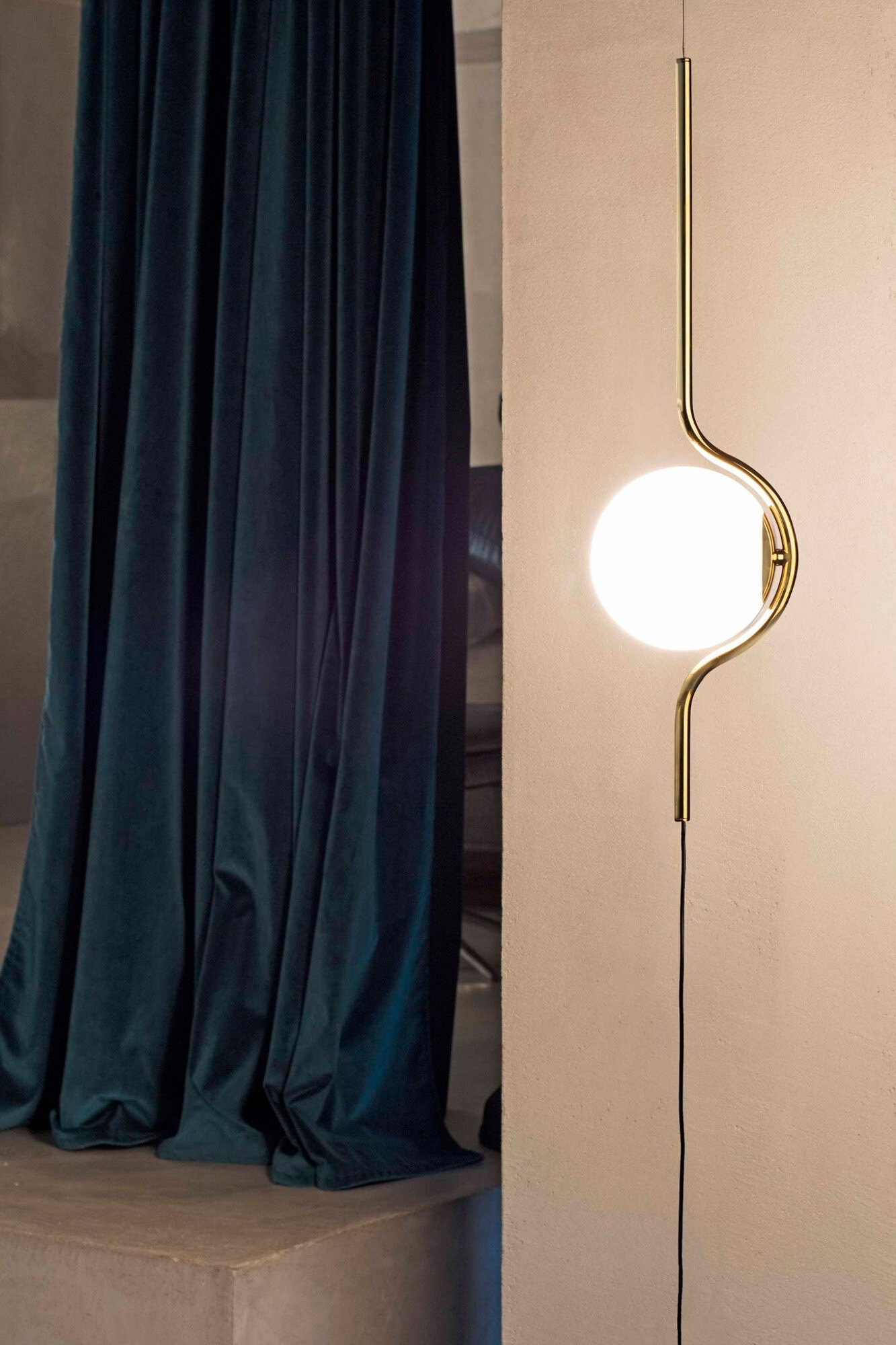 Una lampada dorata con una sfera luminosa bianca e rotonda su un muro.