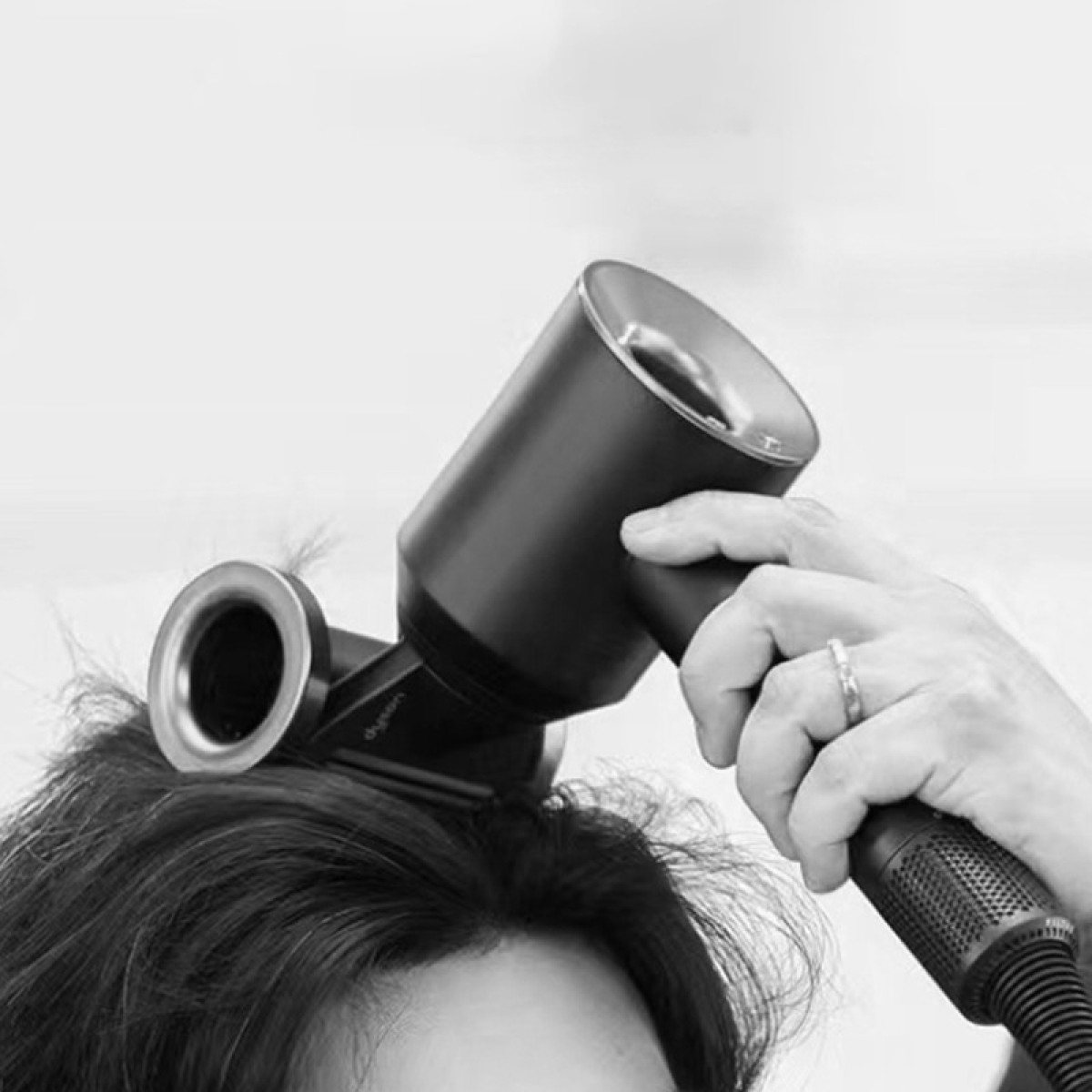 Hand trocknet dunkles Haar mit einem schwarzen Haartrockner, der auf den Kopf gerichtet ist.