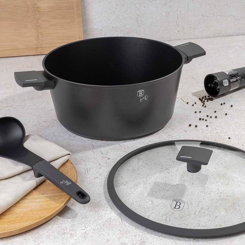 Schwarzer Topf mit Griffen, daneben Kochlöffel, Deckel und Pfeffermühle.