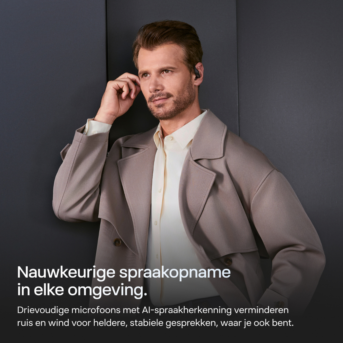 Uomo in cappotto e camicia beige si tocca l'orecchio, indossa auricolari.