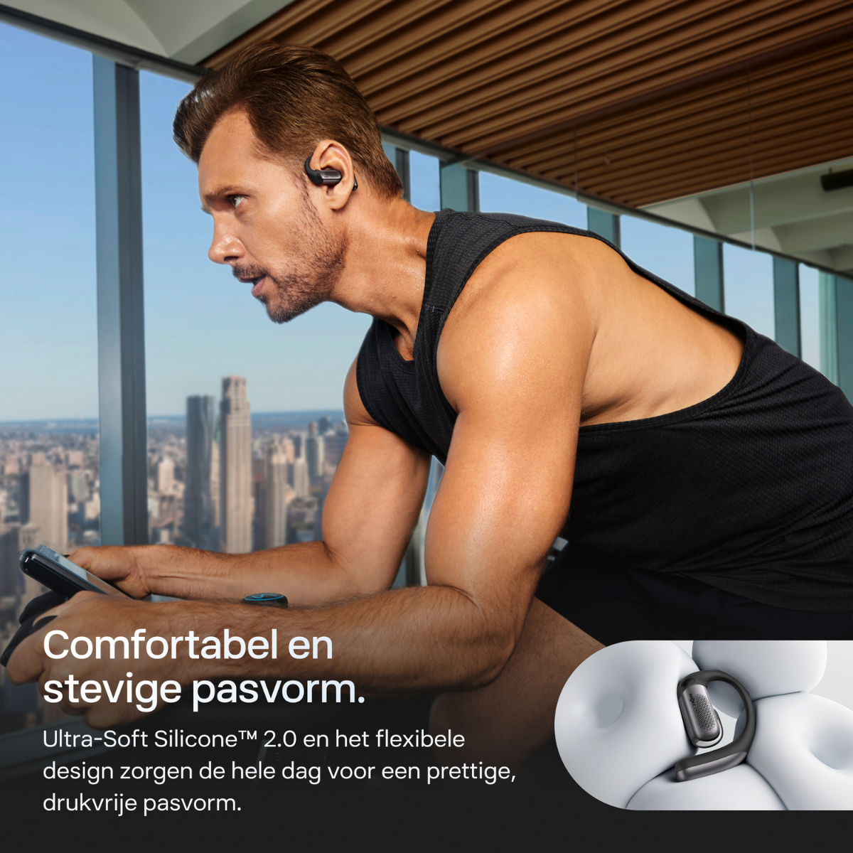 Un uomo si allena in palestra, indossa auricolari. Vista della città sullo sfondo.
