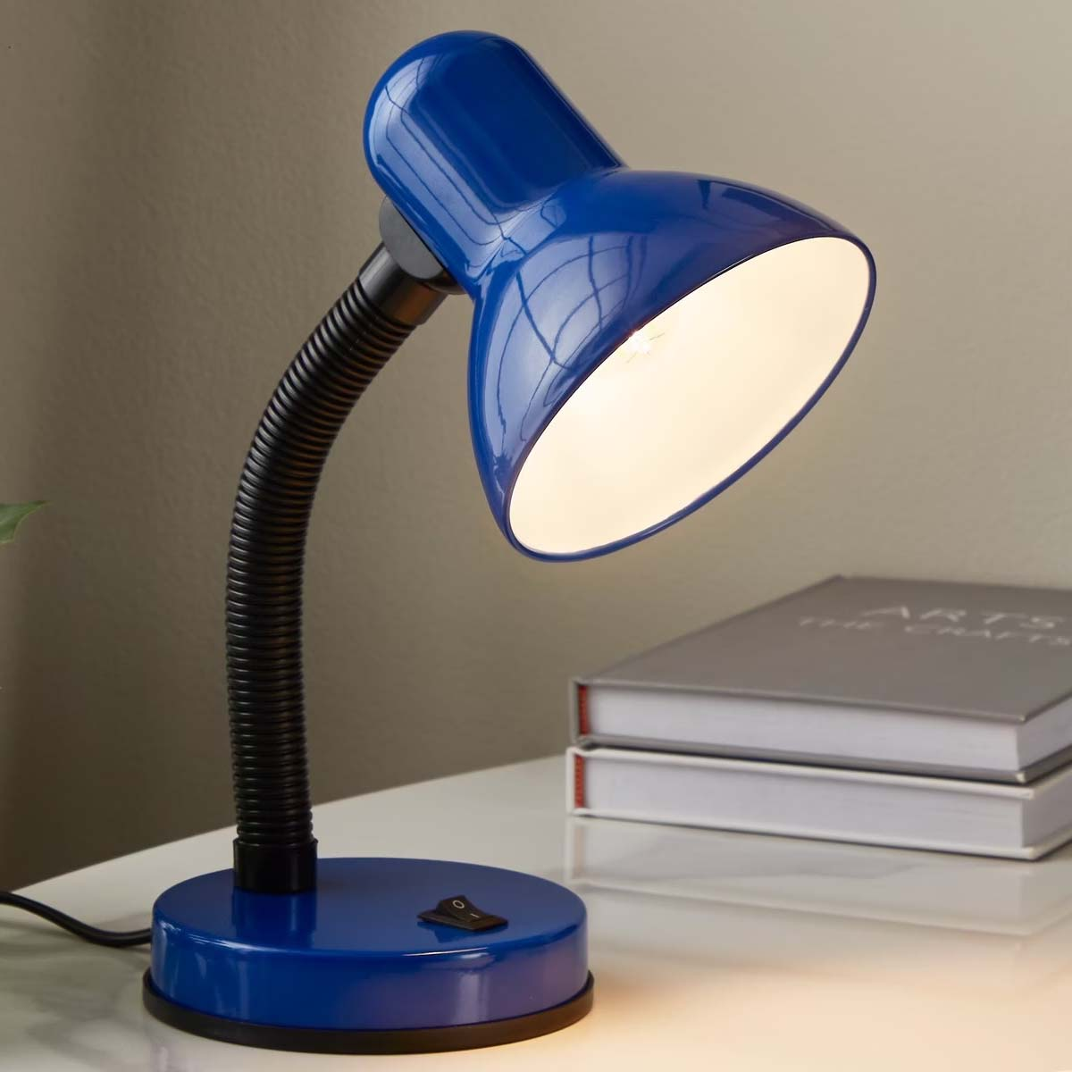 Una lámpara de escritorio azul con brazo flexible y interruptor negro está sobre una mesa.