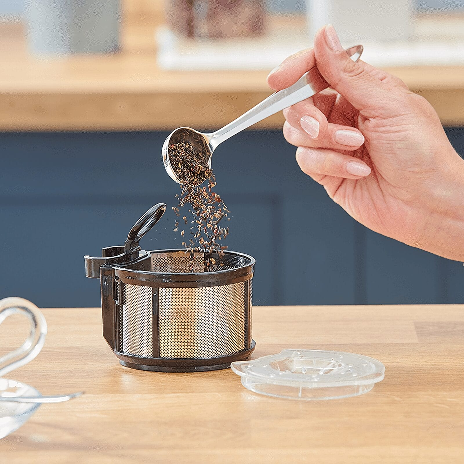 Ręka wsypuje luźną herbatę z łyżki do sitka na herbatę na drewnianym stole.