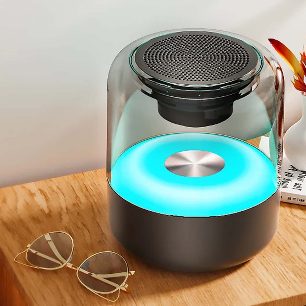 Ein runder Lautsprecher mit blauem Licht steht neben einer Sonnenbrille auf einem Holztisch.