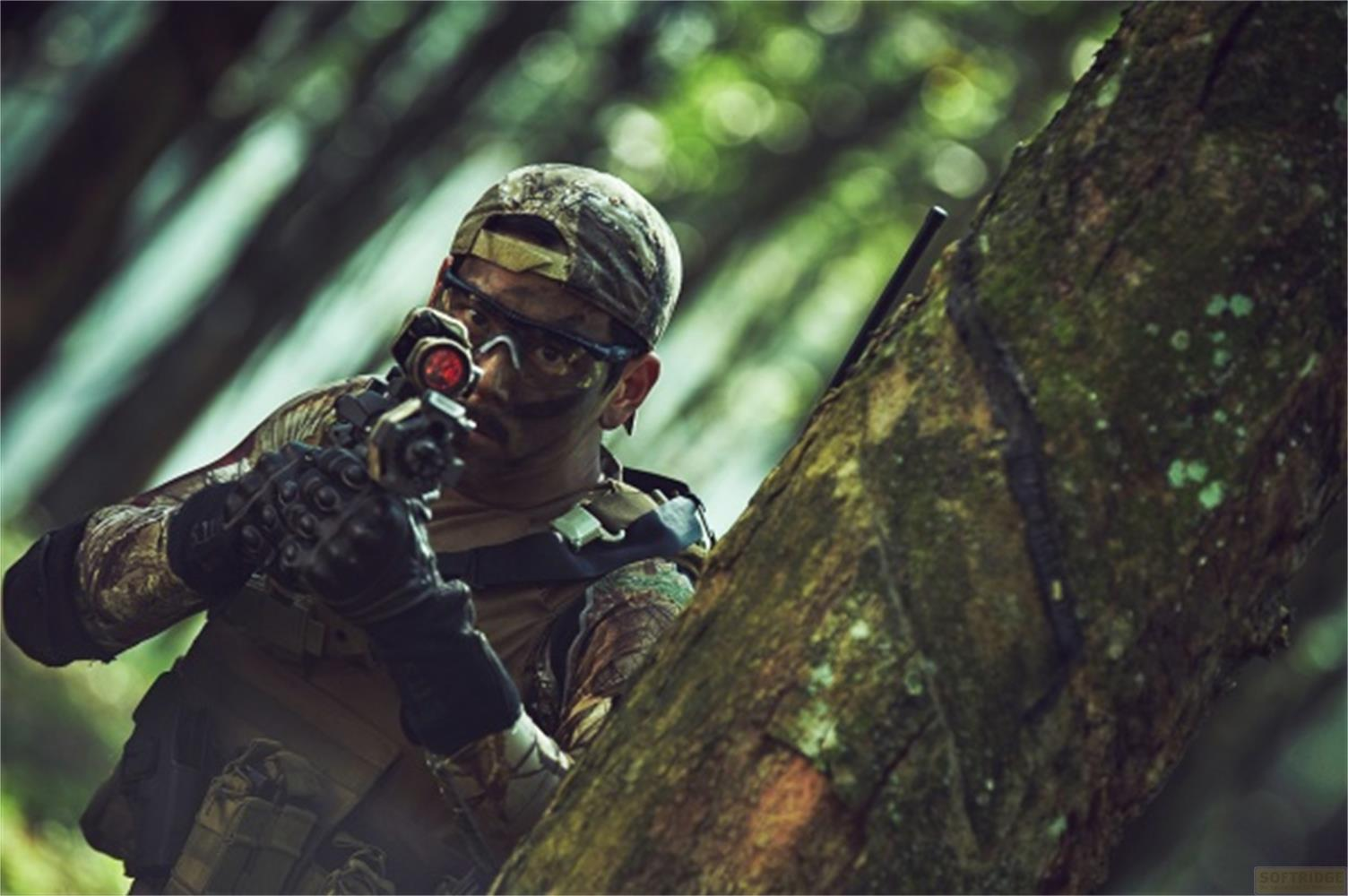 Un soldato in mimetica punta un'arma in una foresta.