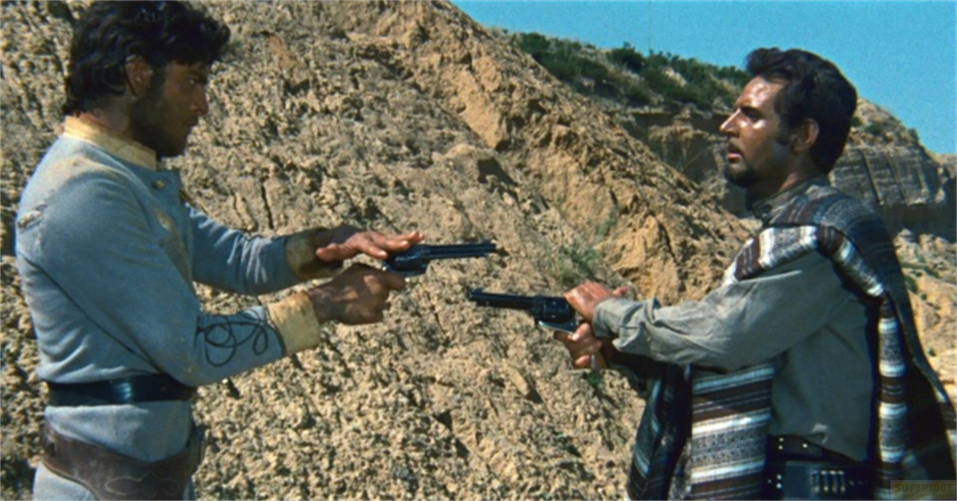 Due uomini in un paesaggio roccioso si puntano i revolver.