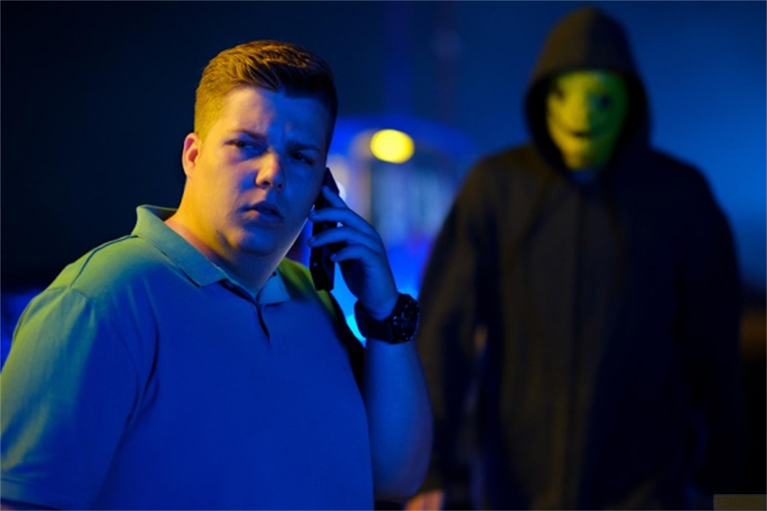 Uomo al telefono, persona con maschera sullo sfondo.