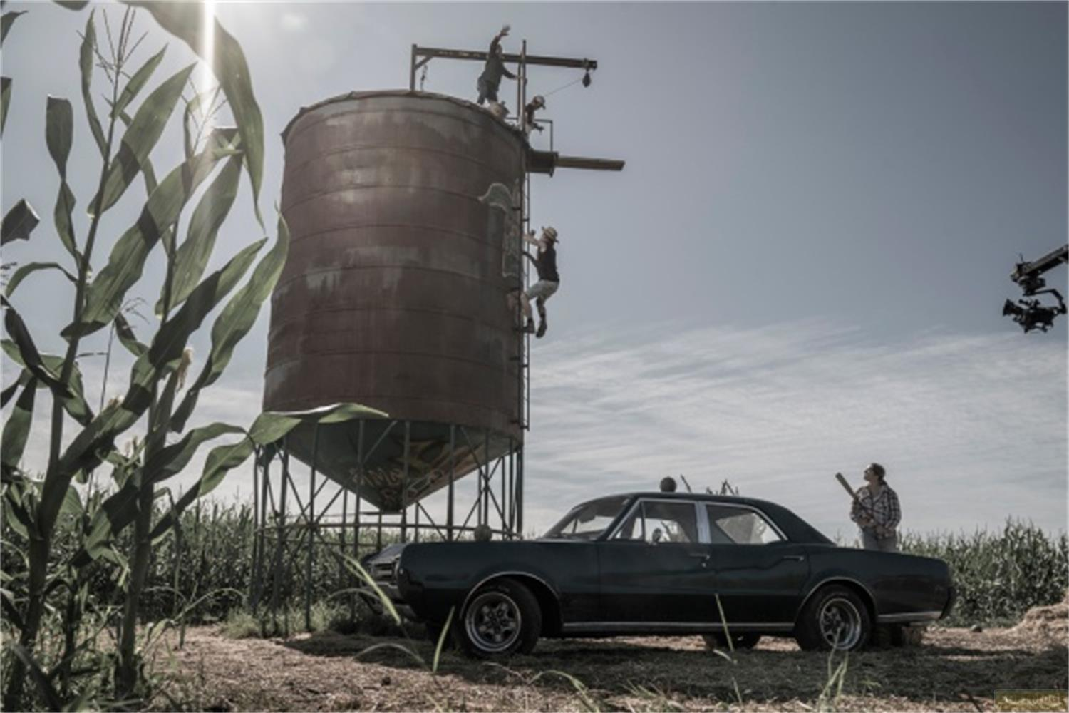 Persone si arrampicano su un silo arrugginito, un'auto parcheggiata.