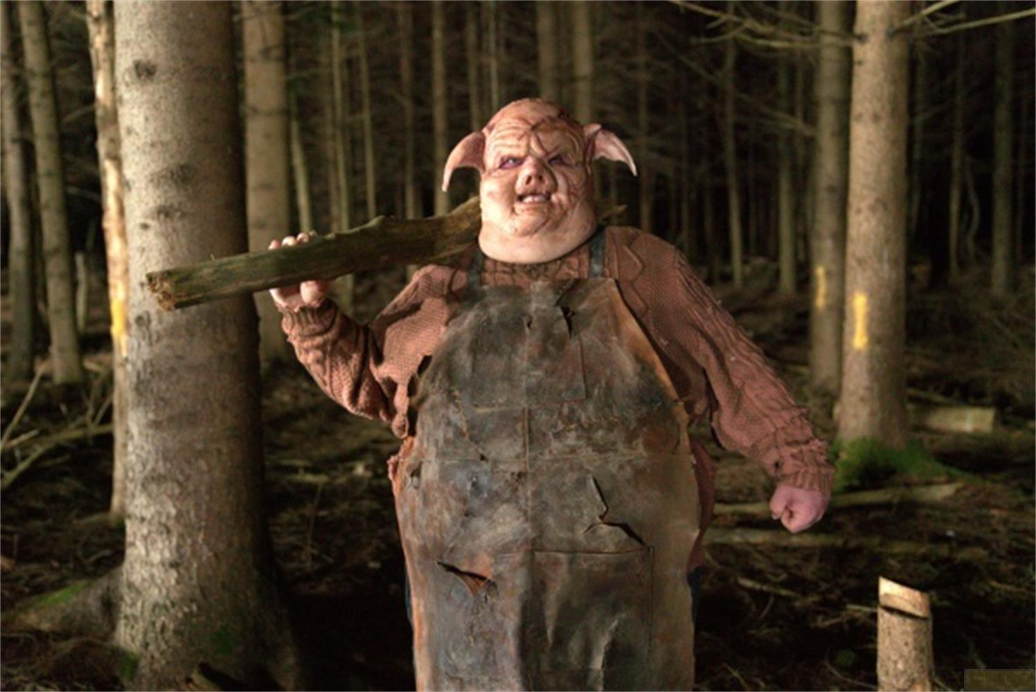 Una persona in costume da maiale con salopette e maglione tiene un ramo in un bosco.