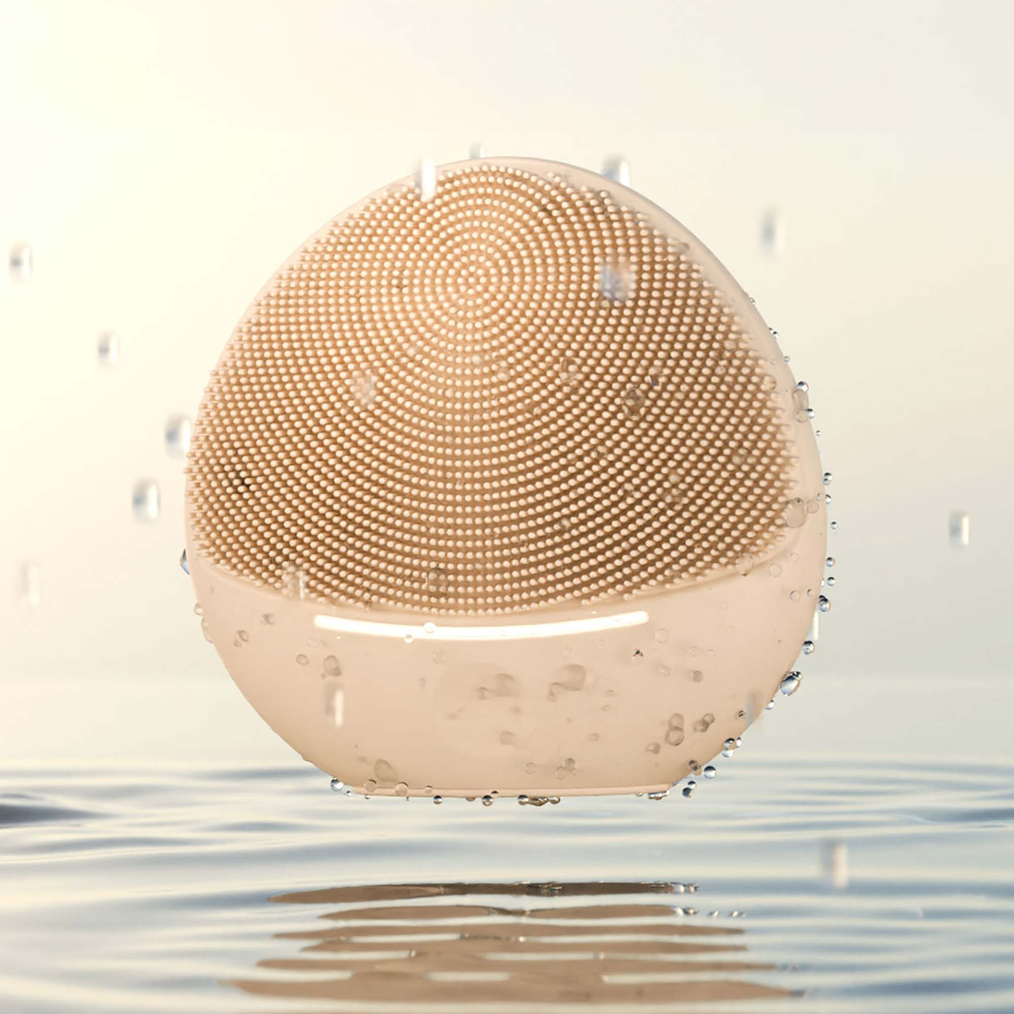 Różowy przyrząd do oczyszczania twarzy z silikonowymi włoskami nad wodą z kroplami.