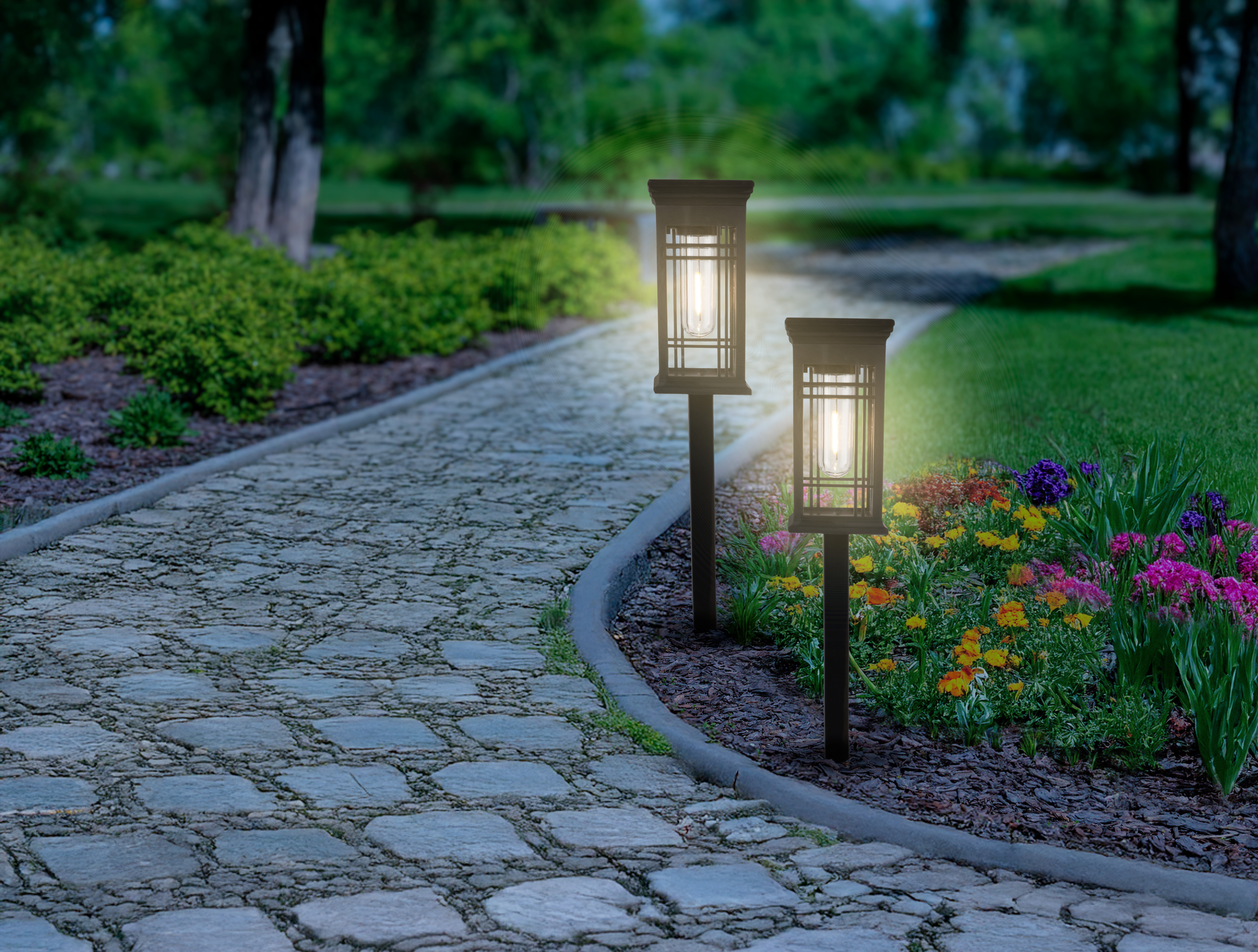 Beleuchteter Gartenweg mit Blumen und Laternen bei Nacht.