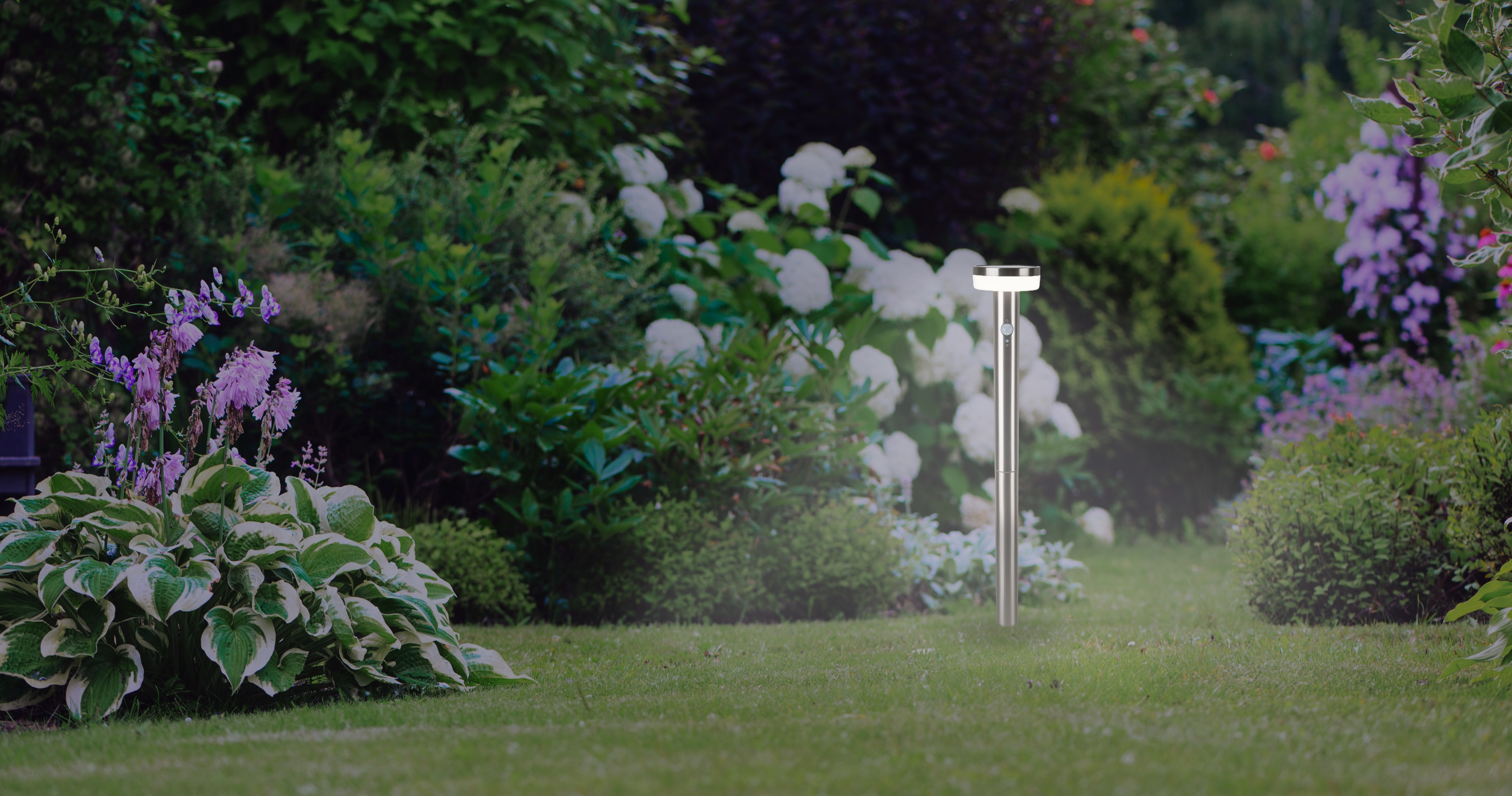 Moderner Gartenpfosten steht im Rasen neben bunten Blumen und Gräsern.