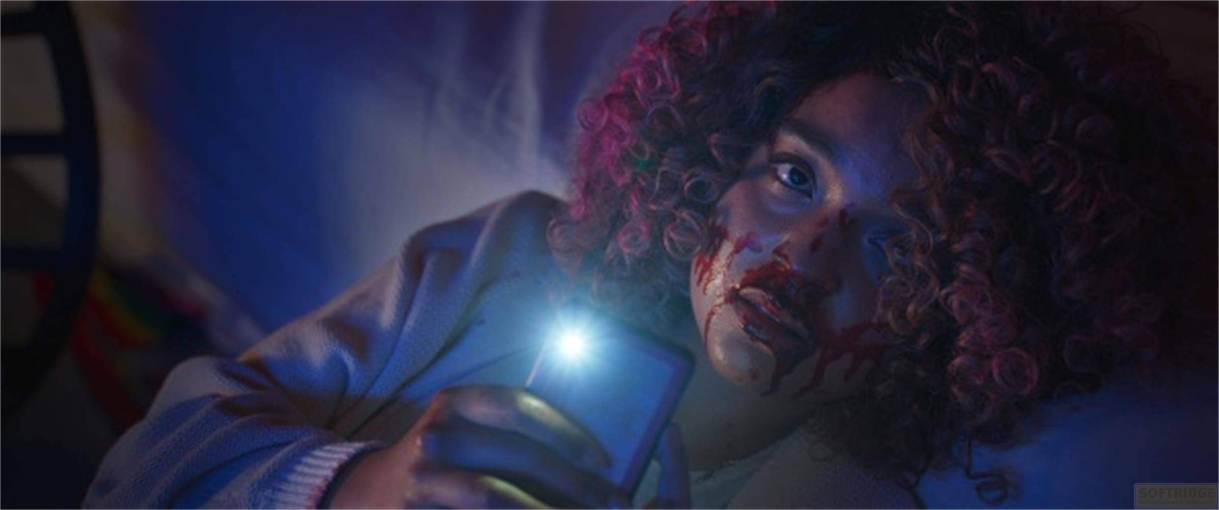 Una donna con il viso insanguinato tiene uno smartphone con la torcia accesa.