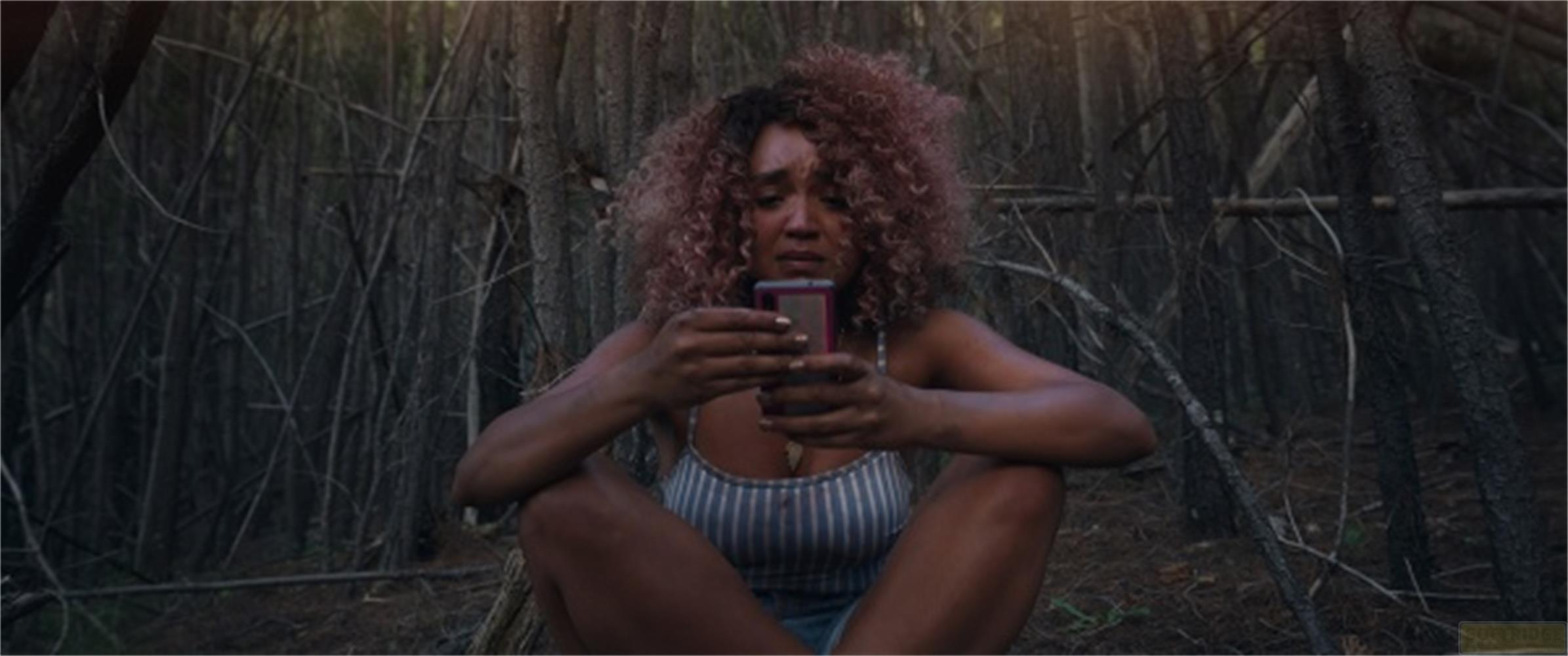 Una donna con i capelli ricci siede in una foresta tenendo un cellulare.