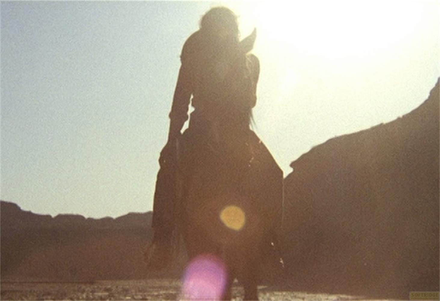 Silhouette di una persona a cavallo di fronte a cielo soleggiato e montagne.