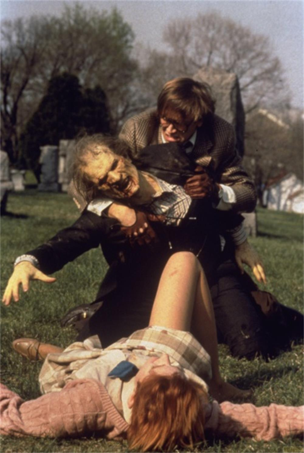 Un uomo lotta con uno zombie in un cimitero mentre una donna giace a terra.