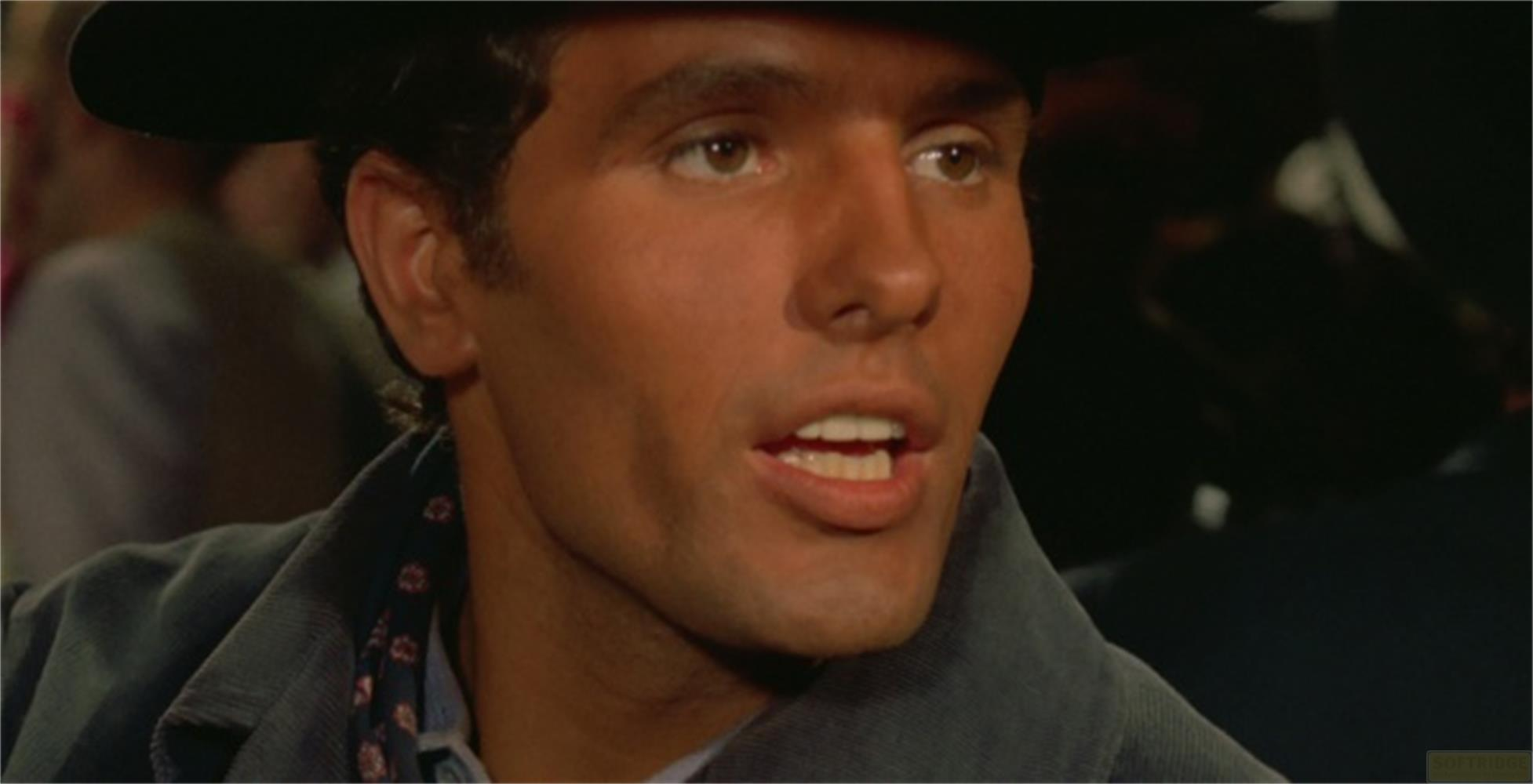 Un uomo con cappello e camicia scura parla.