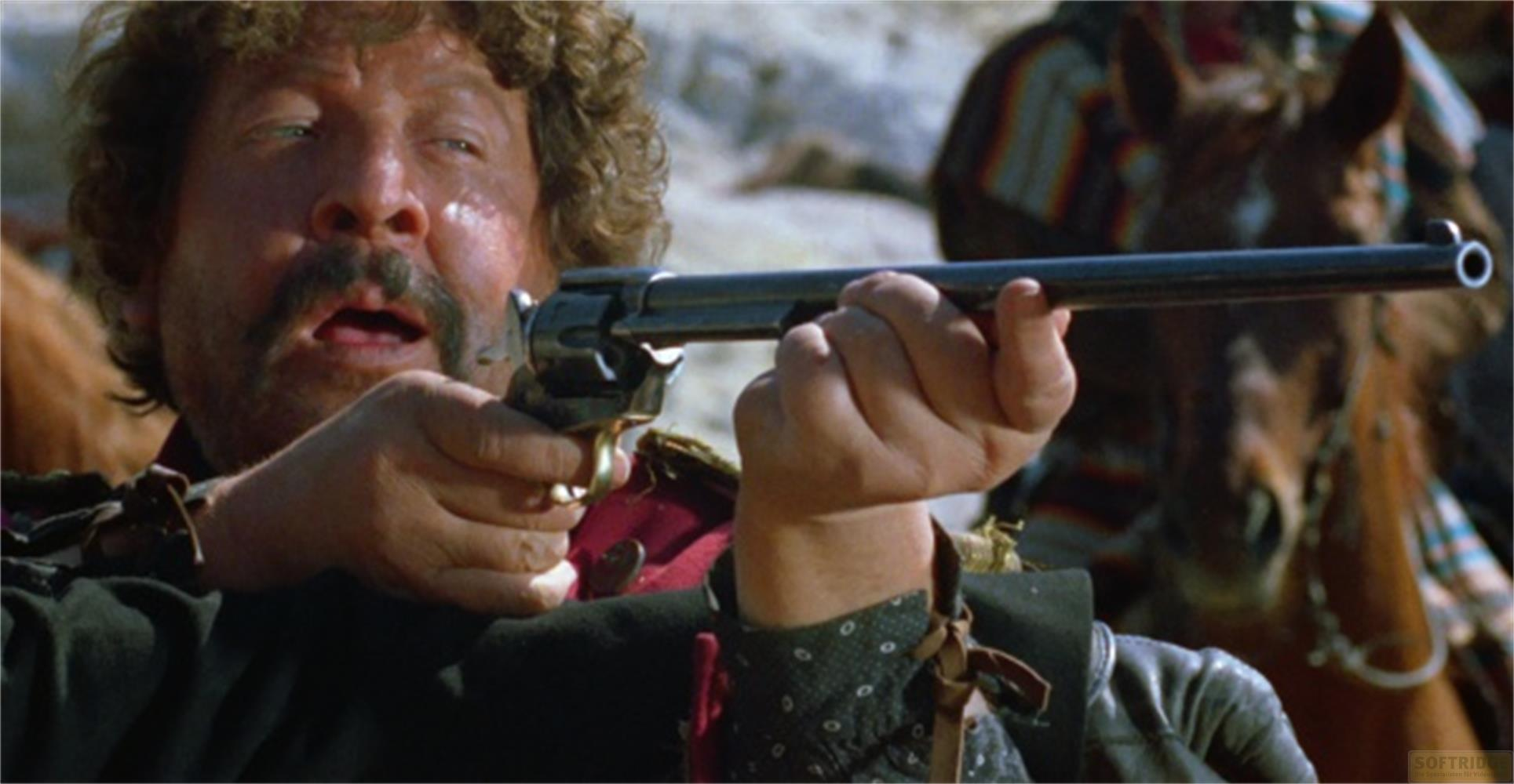 Uomo con baffi mira un revolver. Un cavallo è visibile sullo sfondo.